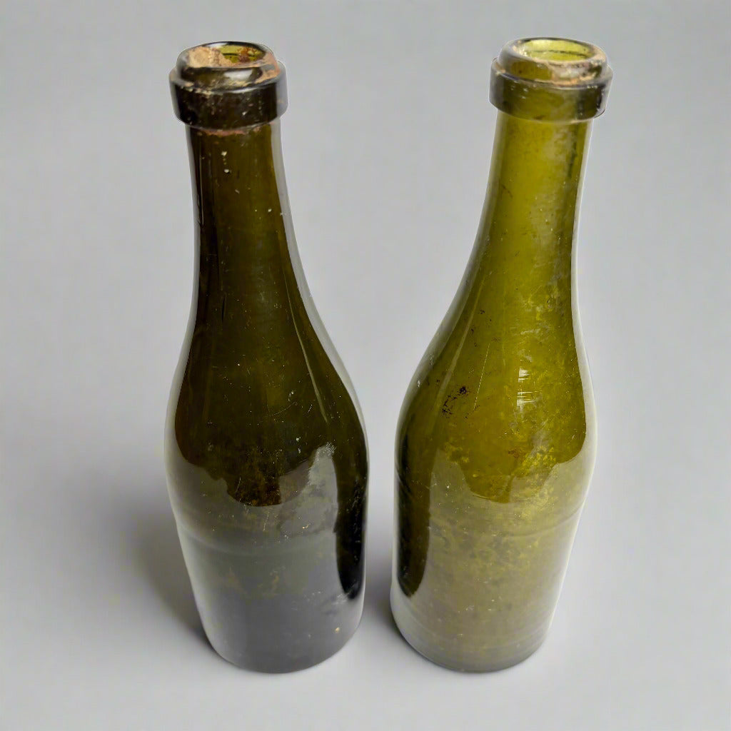 Two old green glass bottles with black caps on a white background