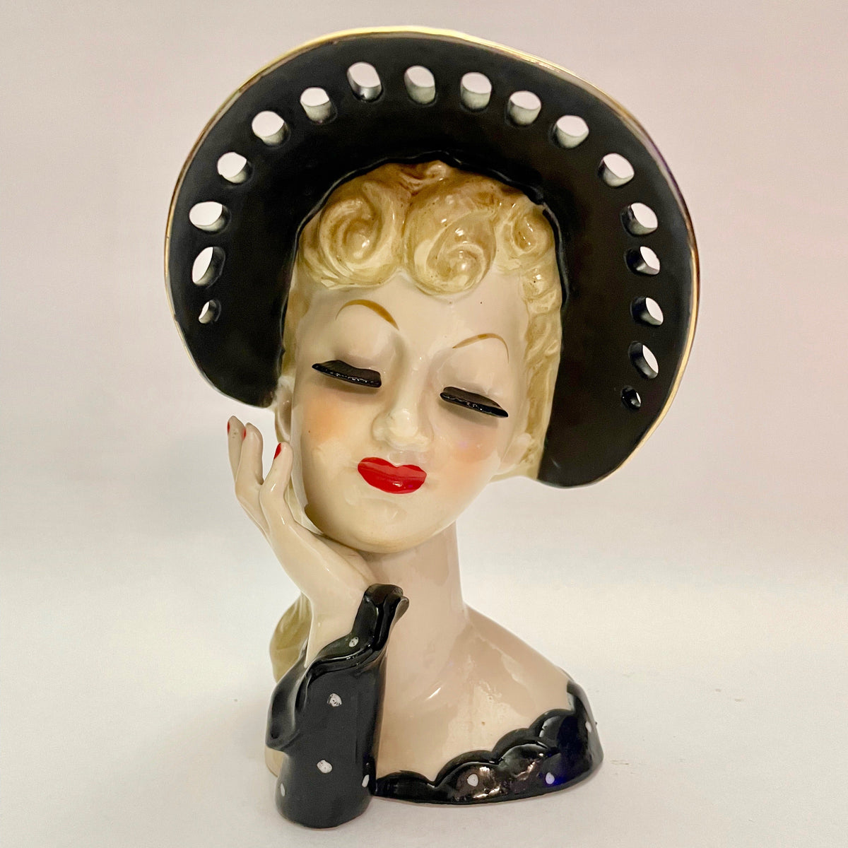 Decorative ceramic bust of a woman wearing a black hat with white dots on a beige background