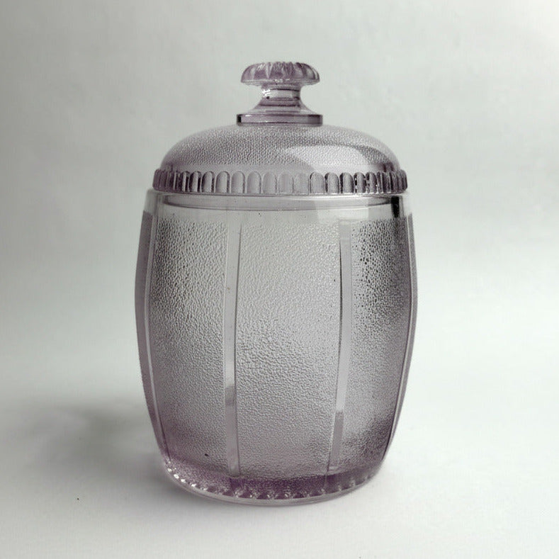 Clear glass jar with a textured surface and silver lid on a light gray background
