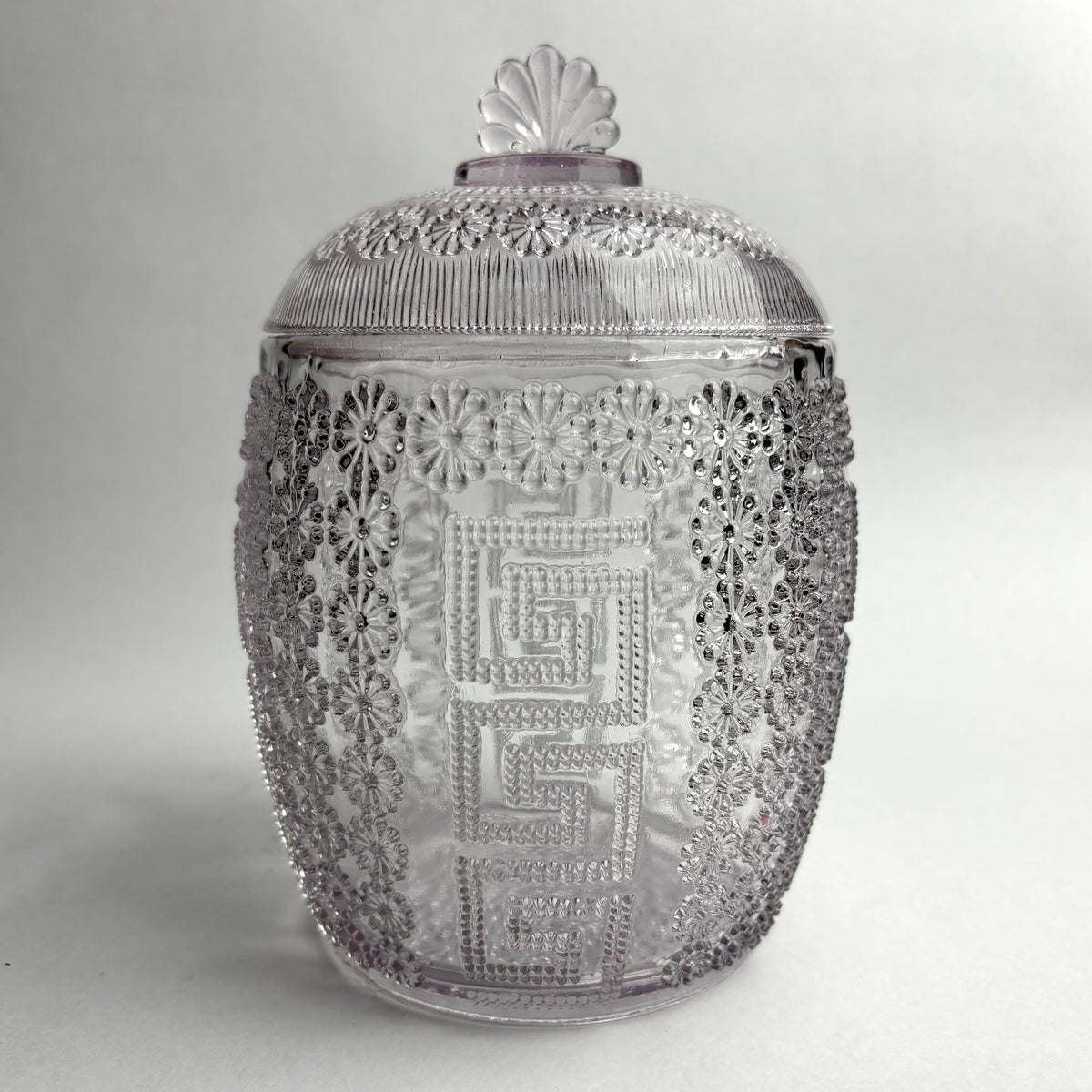 A purple glass honey barrel featuring an intricate geometric and floral pattern, with a honeycomb design and a daisy motif on the lid, suggestive of a vintage or antique style.