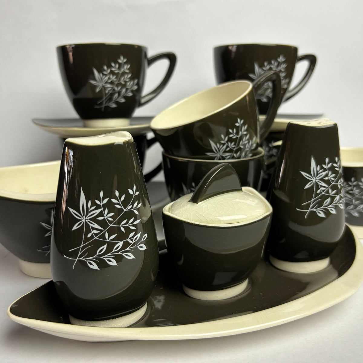 A set of hand-painted 'Boomerang' tea set in charcoal and white, featuring a design with leaves and geometric patterns.