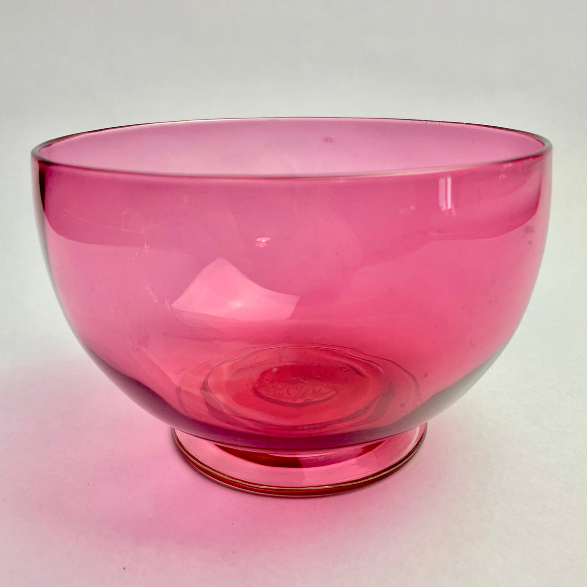 A round, cranberry red glass bowl with a smooth finish on a plain background.