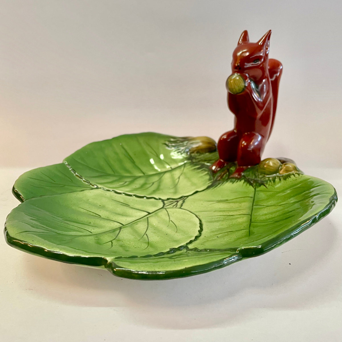 A ceramic Wembley Ware squirrel platter with a green leaf pattern and a red squirrel in the center.