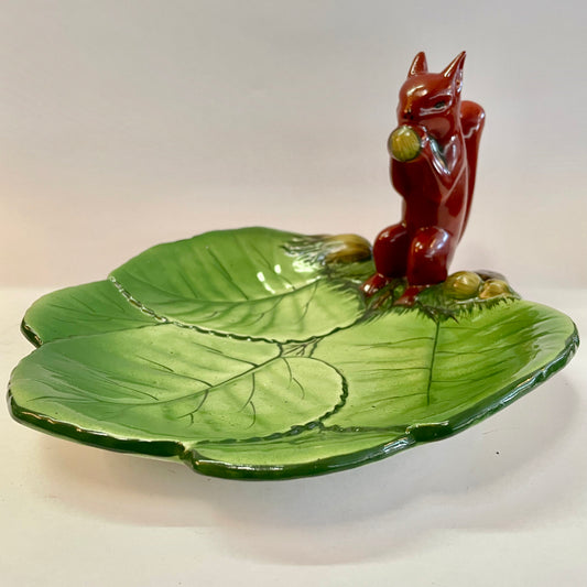 A ceramic Wembley Ware squirrel platter with a green leaf pattern and a red squirrel in the center.