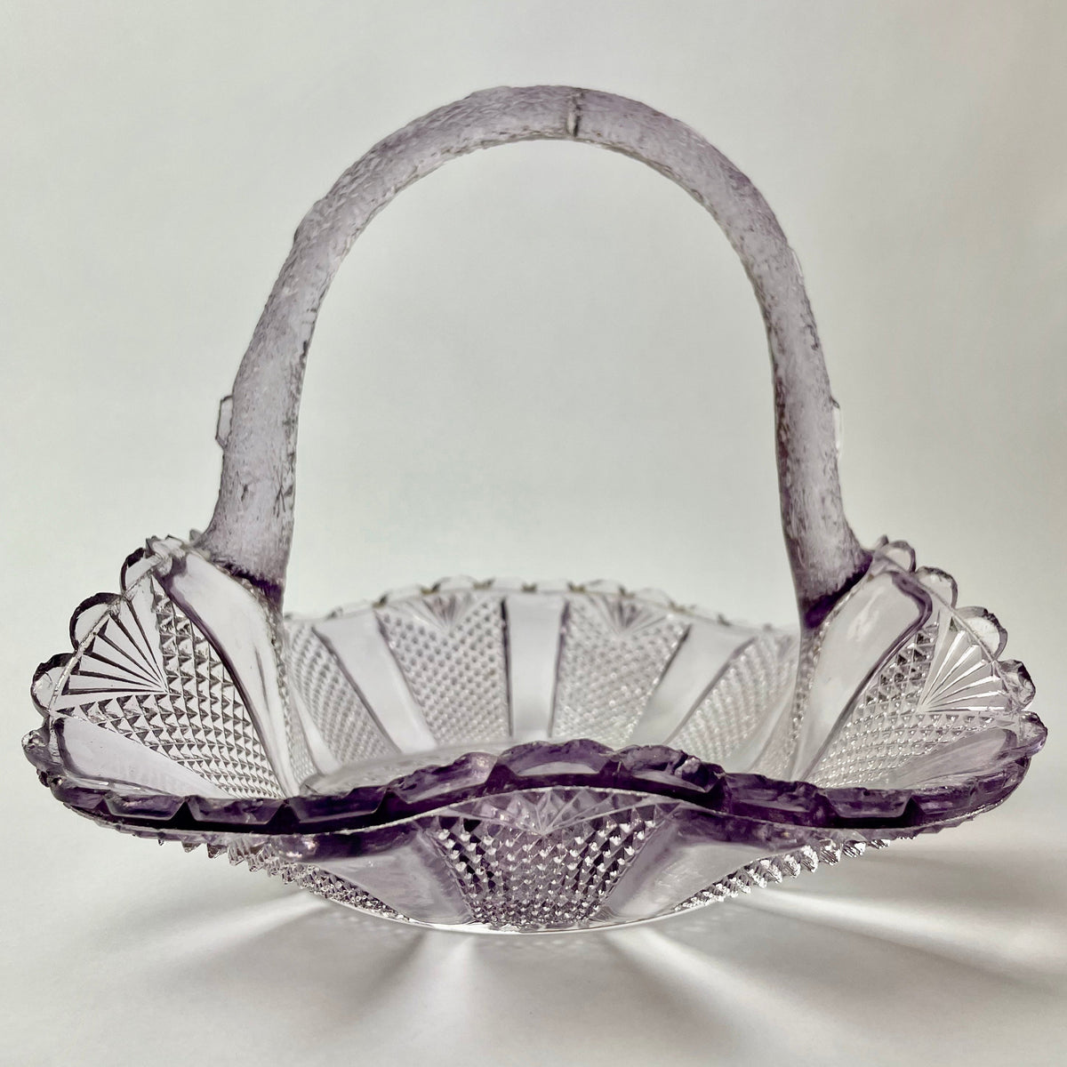 A purple amethyst glass basket with a floral pattern, showing some signs of wear.
