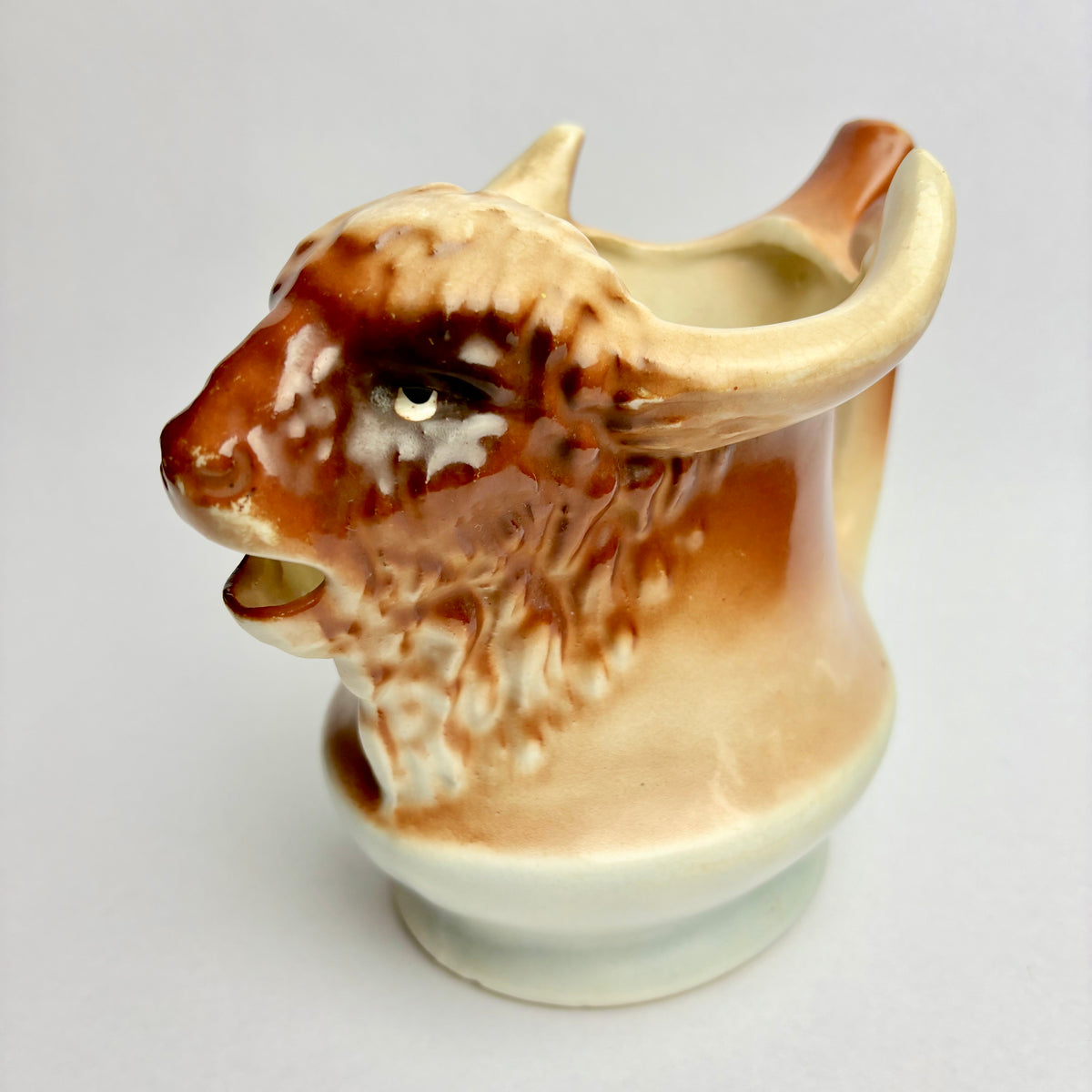 A ceramic pitcher in the shape of a bison, predominantly beige and brown in color, with a vintage appearance.