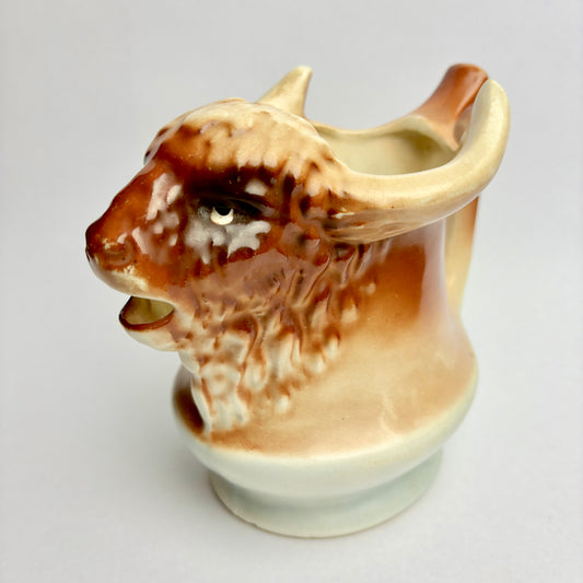 A ceramic pitcher in the shape of a bison, predominantly beige and brown in color, with a vintage appearance.